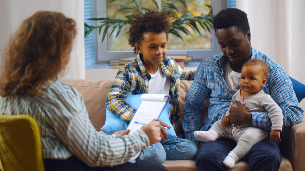 Social worker consulting smiling young single father with kids at home.