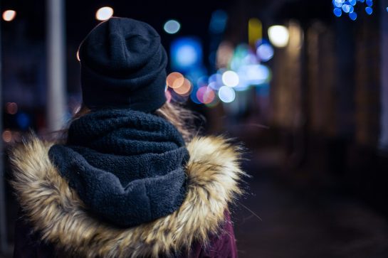 Back view of a hipster girl walking on city street at night