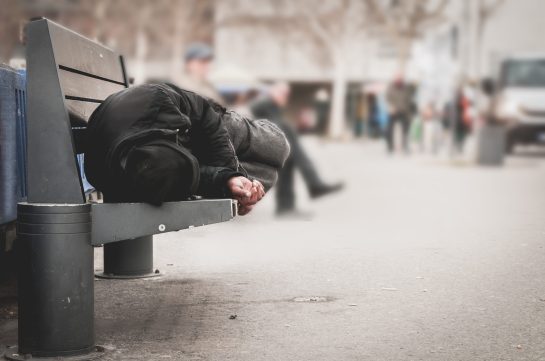 Poor homeless man or refugee sleeping on the wooden bench on the