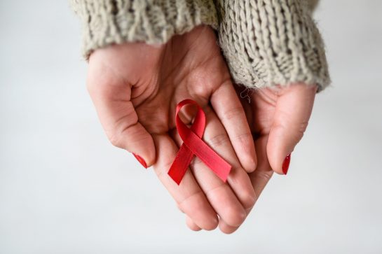 Woman holding red ribbon on her palms. AIDS awareness symbol