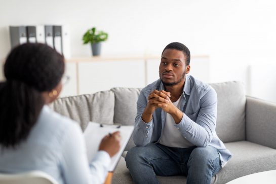 Psychological help service. Depressed black male patient having psychotherapy session with counselor at mental health clinic. Young man with emotional problems consulting professional therapist